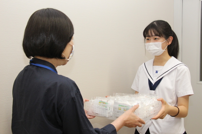 手作りマスクを子育て支援課長に手渡す久保田さんの写真